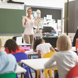 Teacher explaining to school kids human body thanks to a dummy human skeleton.